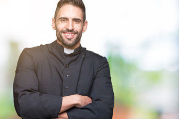 Young Christian priest over isolated background happy face smiling with crossed arms looking at the...