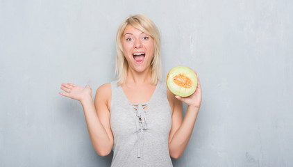 Adult caucasian woman over grunge grey wall eating cantaloupe melon very happy and excited, winner expression celebrating victory screaming with big smile and raised hands