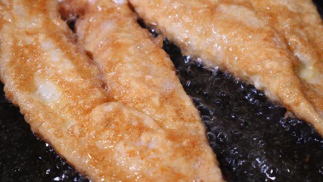 Battered fish, frying in hot oil on a pan