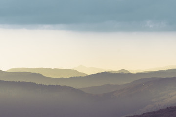 Majestic landscape of summer mountains. A view of the misty slopes of the mountains in the distance. Morning misty coniferous forest hills in fog and rays of sunlight.Travel background.