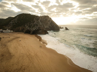 Aerial view from a sandy beach at the sunset with an amazing cliff. Adraga beach Sintra, Portugal