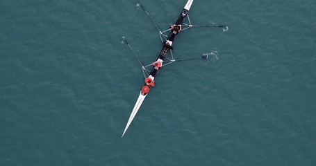 A lock down drone footage above a river filming a rowing team as it is rowing across the frame and leaves the scene. 4k 4096x2160 pixels