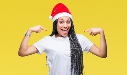 Young braided hair african american girl wearing christmas hat over isolated background looking confident with smile on face, pointing oneself with fingers proud and happy.