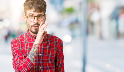 Young handsome man wearing glasses over isolated background hand on mouth telling secret rumor, whispering malicious talk conversation