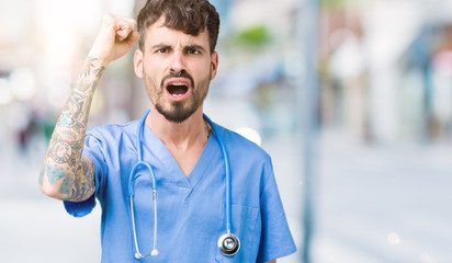 Young handsome nurse man wearing surgeon uniform over isolated background angry and mad raising fist frustrated and furious while shouting with anger. Rage and aggressive concept.