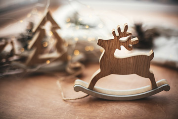 Rustic reindeer christmas toy on wooden table on background of wooden tree,lights, twine, gift in...
