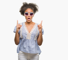 Young afro american woman wearing glasses over isolated background amazed and surprised looking up and pointing with fingers and raised arms.