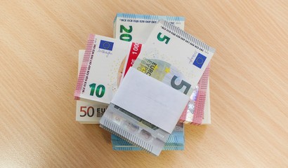 Stacks of Euro bills in fives, tens, fifties and twenties on a pine desk