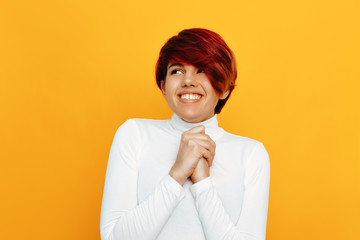 Woman portrait. Emotions. Girl with short red hair is holding hands together, looking upward and...
