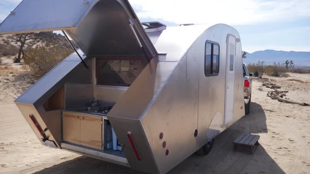A custom built metal teardrop travel trailer tiny house towed by a pickup truck parked at a desert campsite on a road trip across America.