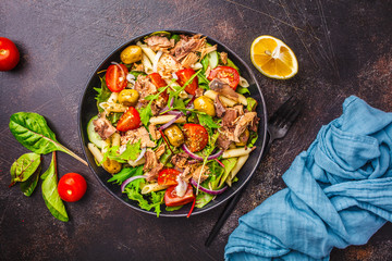 Tuna salad with pasta, olives and vegetables in black plate on dark background.