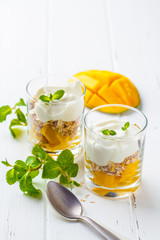 Greek yogurt mango granola parfait in a glass on white wooden background.