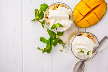 Greek yogurt mango granola parfait in a glass on white wooden background.