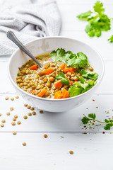 Homemade vegan lentil soup with vegetables and cilantro, white wooden background.