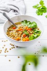 Homemade vegan lentil soup with vegetables and cilantro, white wooden background.