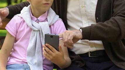 Little boy teaching his grandfather using smart phone to make a call, technology