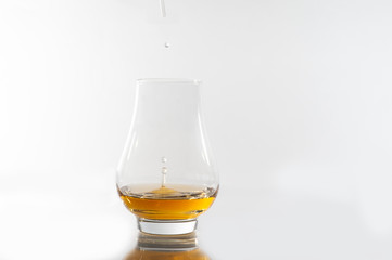 Drops of water being added to a glass of whisky, neutral white surface