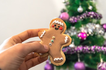 Close-up of a hand holding a homemade christmas cookie with blurred Christmas tree with lights in the background. Home with christmas decoration.