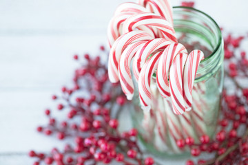Christmas photograph of candy canes in a green mason jar with red berries on white