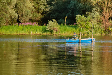 Naklejka premium Novi Sad, Serbia - August 04, 2018: Danube island (Šodroš) near Novi Sad, Serbia. Fishermans sitting in boat and holding fishing rod.