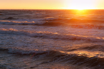 Fototapeta premium Sunset over the sea. Reflection of sunlight in the sea waves. Red and yellow sky in the rays of the sunset.