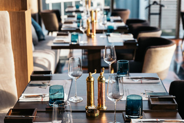 Bronze bottles of salt and pepper on wooden table with blur dining table in background.