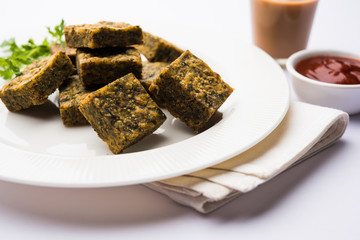 A savory cilantro cake or kothimbir vadi in square shape which is first steamed and then fried until crisp. popular indian snack served with hot tea and tomato ketchup