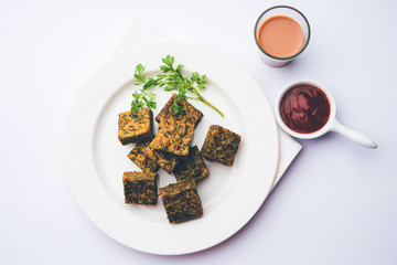 A savory cilantro cake or kothimbir vadi in square shape which is first steamed and then fried until crisp. popular indian snack served with hot tea and tomato ketchup