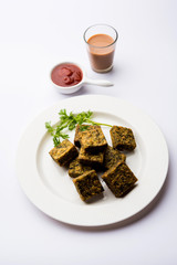 A savory cilantro cake or kothimbir vadi in square shape which is first steamed and then fried until crisp. popular indian snack served with hot tea and tomato ketchup