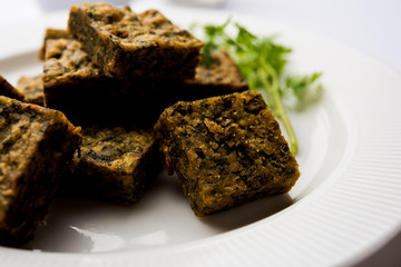 A savory cilantro cake or kothimbir vadi in square shape which is first steamed and then fried until crisp. popular indian snack served with hot tea and tomato ketchup