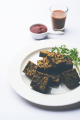 A savory cilantro cake or kothimbir vadi in square shape which is first steamed and then fried until crisp. popular indian snack served with hot tea and tomato ketchup