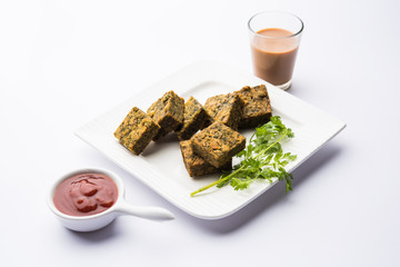 A savory cilantro cake or kothimbir vadi in square shape which is first steamed and then fried until crisp. popular indian snack served with hot tea and tomato ketchup
