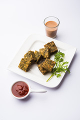 A savory cilantro cake or kothimbir vadi in square shape which is first steamed and then fried until crisp. popular indian snack served with hot tea and tomato ketchup