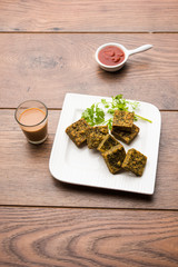 A savory cilantro cake or kothimbir vadi in square shape which is first steamed and then fried until crisp. popular indian snack served with hot tea and tomato ketchup