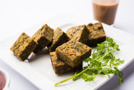 A savory cilantro cake or kothimbir vadi in square shape which is first steamed and then fried until crisp. popular indian snack served with hot tea and tomato ketchup