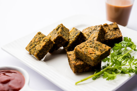 A savory cilantro cake or kothimbir vadi in square shape which is first steamed and then fried until crisp. popular indian snack served with hot tea and tomato ketchup