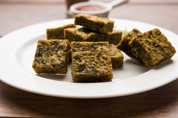 A savory cilantro cake or kothimbir vadi in square shape which is first steamed and then fried until crisp. popular indian snack served with hot tea and tomato ketchup