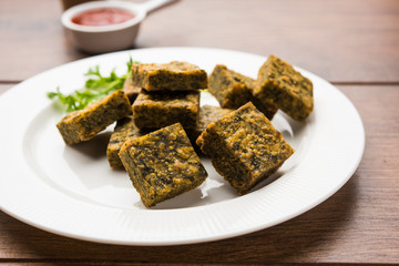 A savory cilantro cake or kothimbir vadi in square shape which is first steamed and then fried until crisp. popular indian snack served with hot tea and tomato ketchup