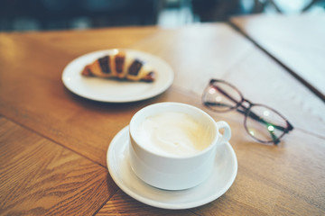 Quick Breakfast with coffee and croissant on the table by the window in modern cafe, copy space