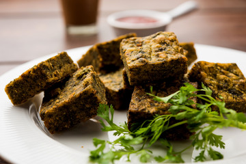 A savory cilantro cake or kothimbir vadi in square shape which is first steamed and then fried until crisp. popular indian snack served with hot tea and tomato ketchup