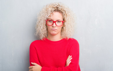 Young blonde woman with curly hair over grunge grey background skeptic and nervous, disapproving...