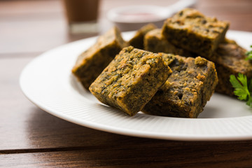 A savory cilantro cake or kothimbir vadi in square shape which is first steamed and then fried until crisp. popular indian snack served with hot tea and tomato ketchup