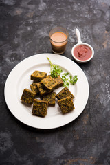 A savory cilantro cake or kothimbir vadi in square shape which is first steamed and then fried until crisp. popular indian snack served with hot tea and tomato ketchup
