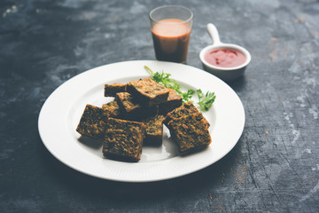 A savory cilantro cake or kothimbir vadi in square shape which is first steamed and then fried until crisp. popular indian snack served with hot tea and tomato ketchup