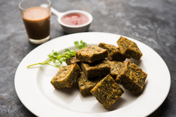 A savory cilantro cake or kothimbir vadi in square shape which is first steamed and then fried until crisp. popular indian snack served with hot tea and tomato ketchup