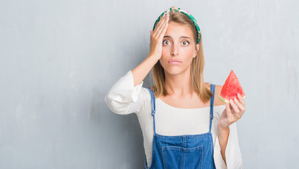 Beautiful young woman over grunge grey wall eating water melon stressed with hand on head, shocked with shame and surprise face, angry and frustrated. Fear and upset for mistake.