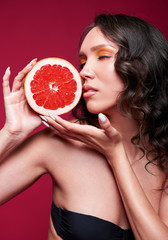 Studio portrait of beautiful smiling young girl with slice of orange (grapefruit) in hands