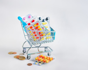 Pills and capsules in the shopping trolley on light background.
