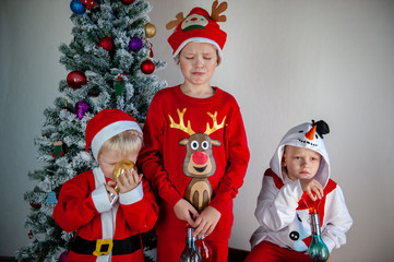 Cute boys dressed in festive costumes of Santa Claus and snowmen and decorate Christmas tree with balls and garlands. Children play and wait for gifts. Christmas Eve