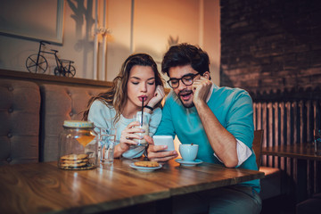  Beautiful loving couple sitting in a cafe drinking coffee and using phone. Love and romance concept.
